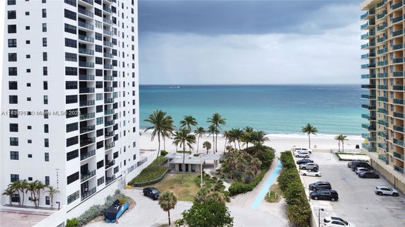 View of tall residential buildings near a beach with ocean in the background.
