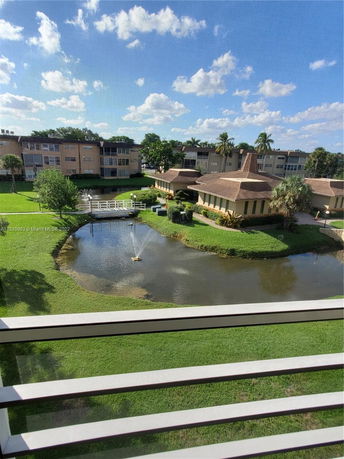 View of residential area with a small pond, fountain, and multiple buildings surrounded by green lawns.