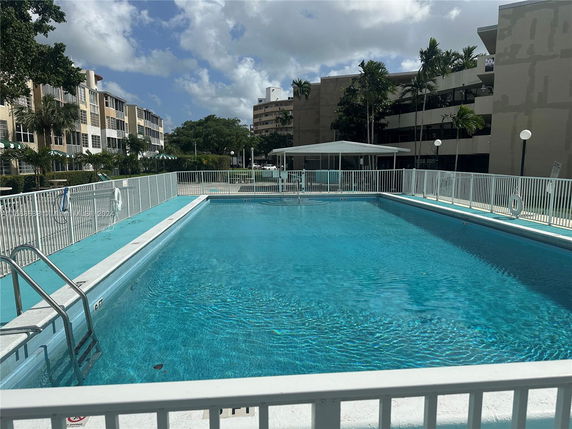 Outdoor swimming pool with a metal fence and ladder, surrounded by residential buildings.