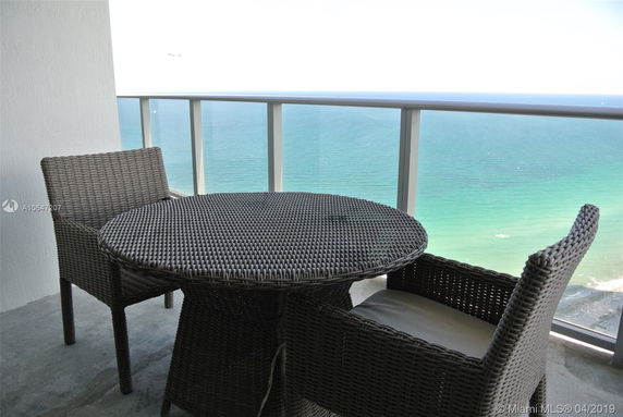 Outdoor wicker table and chairs set on a balcony with a panoramic view of the ocean.