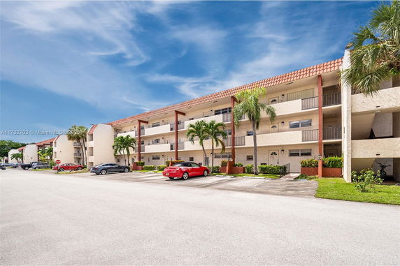 Front view of a multi-story apartment building with balconies and parking area.