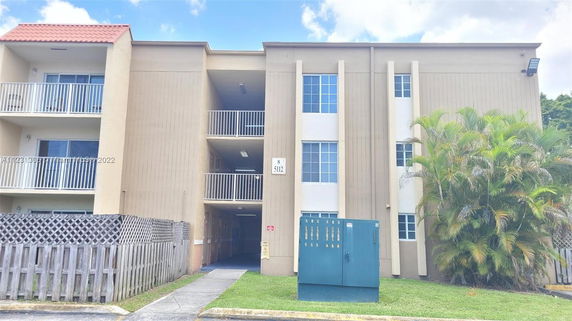 Front view of a multi-story residential building with balconies and a red-tiled roof section.