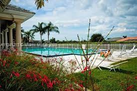 Outdoor swimming pool area with lounge chairs and a railing, surrounded by vegetation and palm trees.