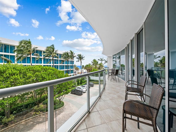 View from a building balcony with glass railing overlooking nearby buildings and palm trees.
