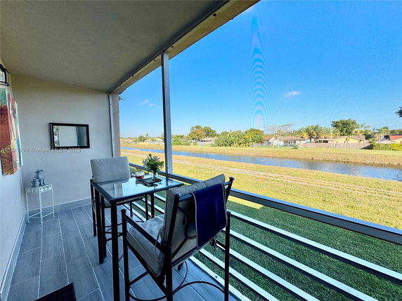 Balcony view overlooking a waterway and grassy area with a table and chairs.