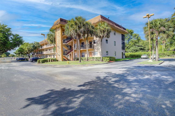 Front view of a multi-story building with an external staircase and surrounding palm trees.