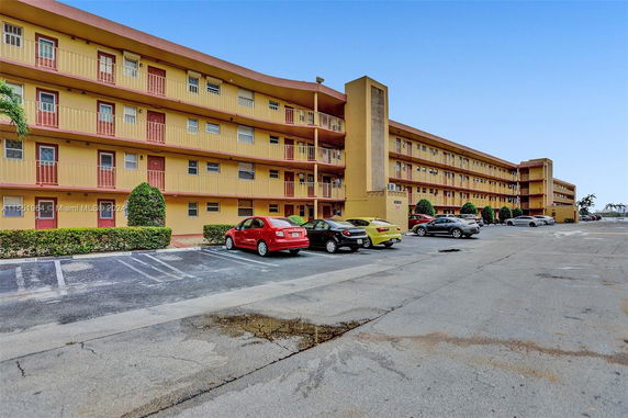 Front view of a multi-story apartment building with balconies and parking area.
