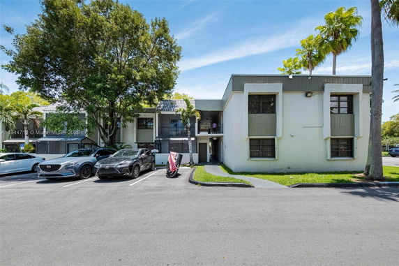 Front view of a two-story building with multiple units and parking area in front.