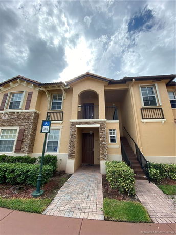Front view of a two-story house with a brick pathway and a balcony.