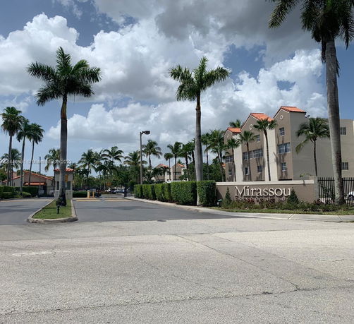 Front view of a residential complex with palm trees and a gated entrance.
