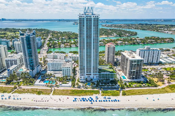 Aerial view of tall beachfront buildings with ocean and inlet.