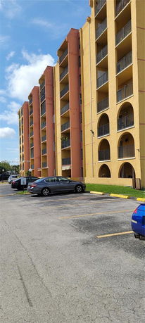 Parking area in front of a multi-story building with yellow and orange facade.
