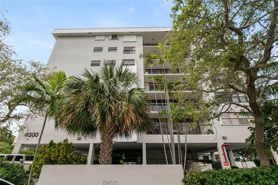 Front view of a multi-story building with balconies and a palm tree in the foreground.