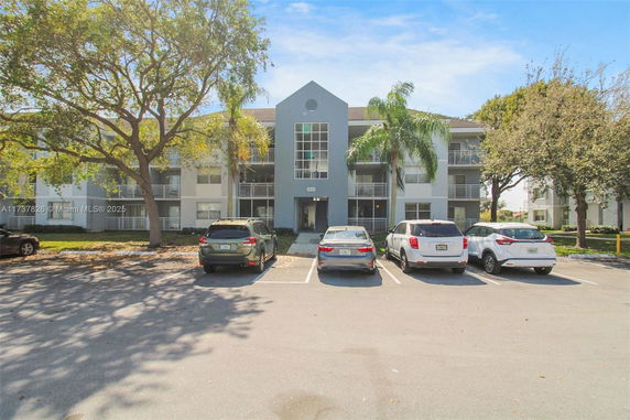 Front view of a multi-story apartment building with balconies and parking area.