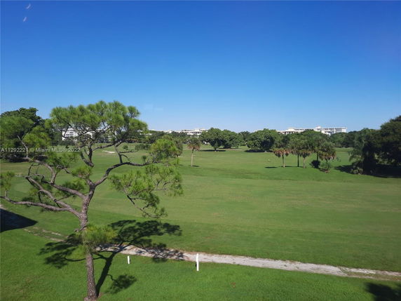 Open grassy area with trees and buildings in the distance under a clear blue sky.