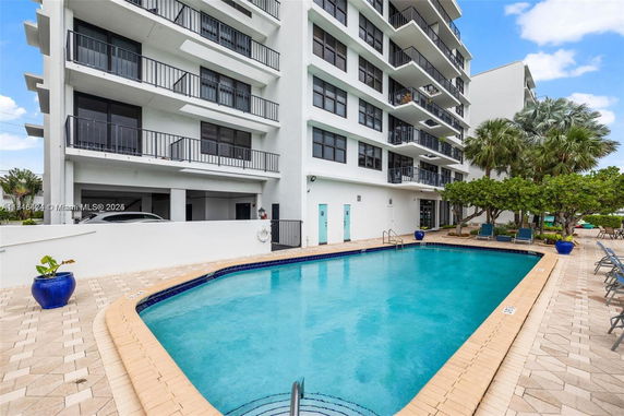 Outdoor swimming pool area adjacent to a multi-story building with balconies.