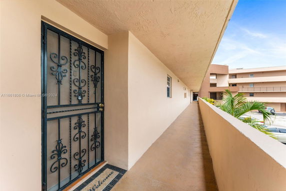 Long exterior hallway of a building with iron door and view of adjacent building.