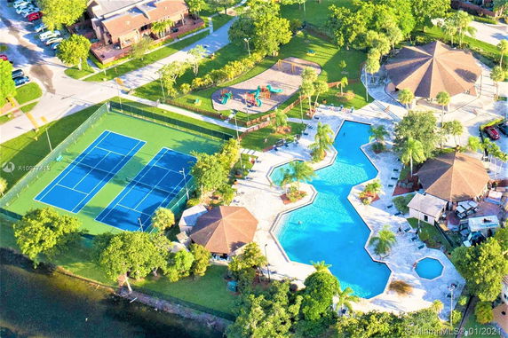Aerial view of a recreational area with tennis courts, swimming pool, and surrounding greenery.
