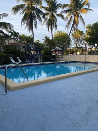 Outdoor swimming pool with surrounding palm trees and patio area.