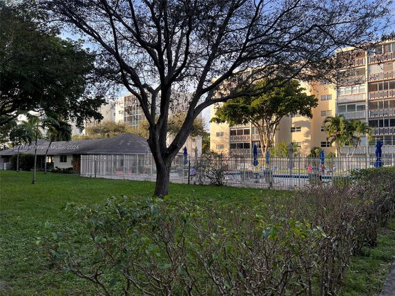Outdoor area with a swimming pool surrounded by a fence and buildings in the background.