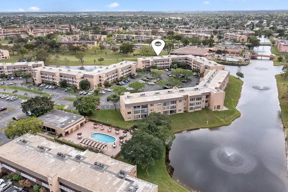 Aerial view of a building complex with a water body and parking area.