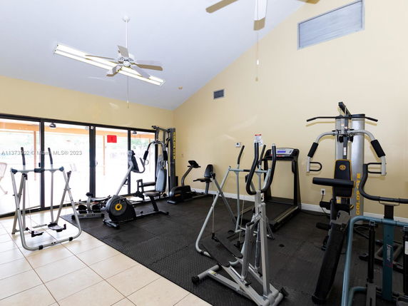 Room equipped with various gym exercise machines and large windows.