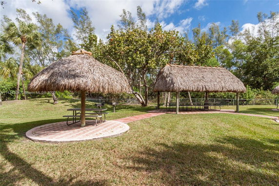 Outdoor area with two thatched-roof structures and picnic tables.