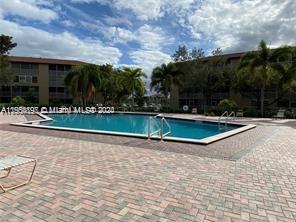Outdoor swimming pool surrounded by brick paving and apartment buildings in the background.