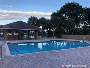 Outdoor swimming pool with a surrounding paved area and a nearby covered structure.