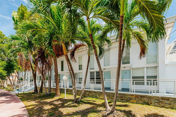 Front view of a modern multi-story building with tall windows and palm trees in front.