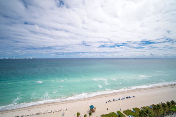 Wide view of a sandy beach and ocean with sun loungers and umbrellas.