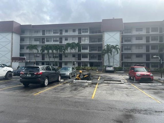 Four-story apartment building with a parking area in front.