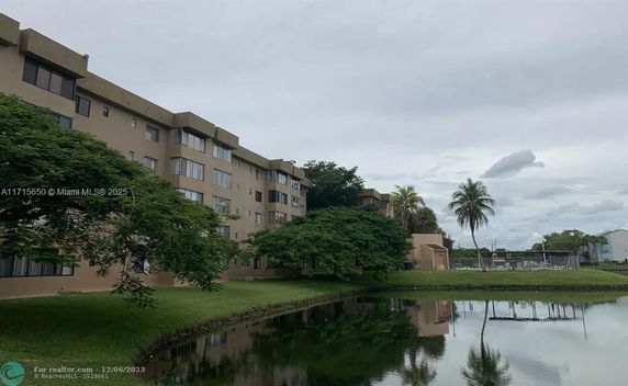 Front view of a multi-story apartment building with large windows and a pond in the foreground.
