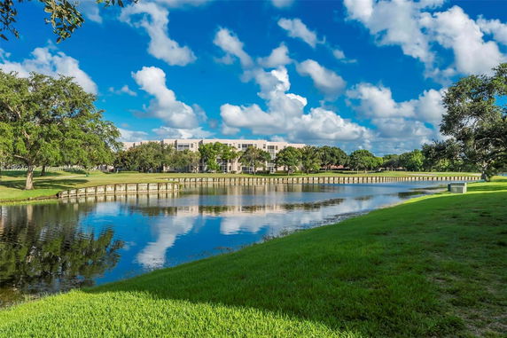 View of a building across a tranquil body of water with grassy areas and trees.