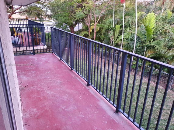 View from a balcony with metal railings overlooking a garden with trees.