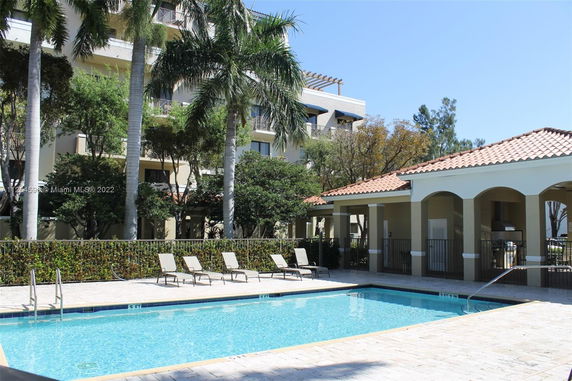 Outdoor view of a swimming pool area with surrounding buildings and palm trees.