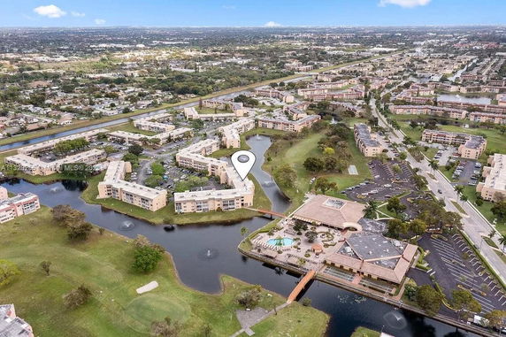 Aerial view of a residential complex with multiple buildings, surrounding water features, and parking areas.