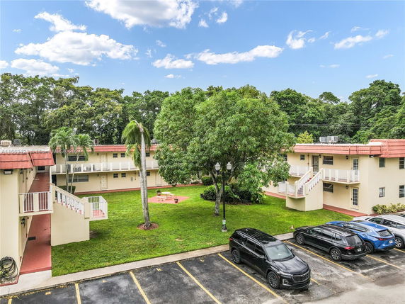 View of a residential complex with two-story buildings surrounding a grassy area and a parking lot with several cars.