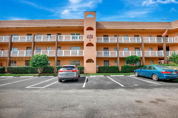 Front view of a three-story building with a parking area and vehicles.