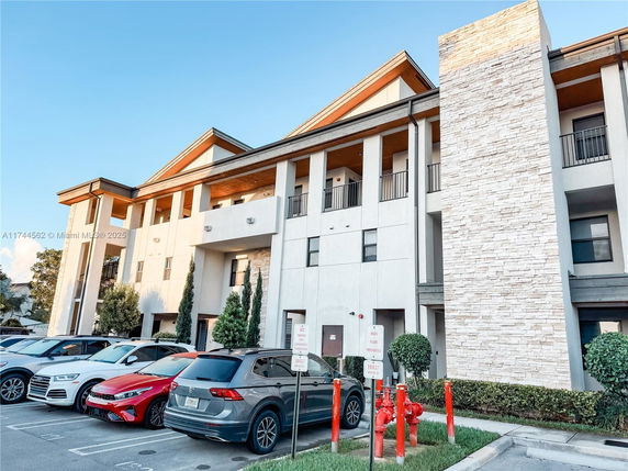 Front view of a multi-story building with balconies and a parking area in front.