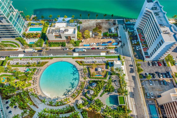 Aerial view of a residential area with a large circular pool, surrounding buildings, and a turquoise body of water.