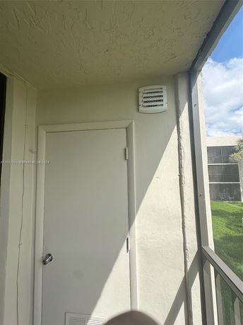 Door and vent on the exterior wall of a building with partial view of balcony and lawn.