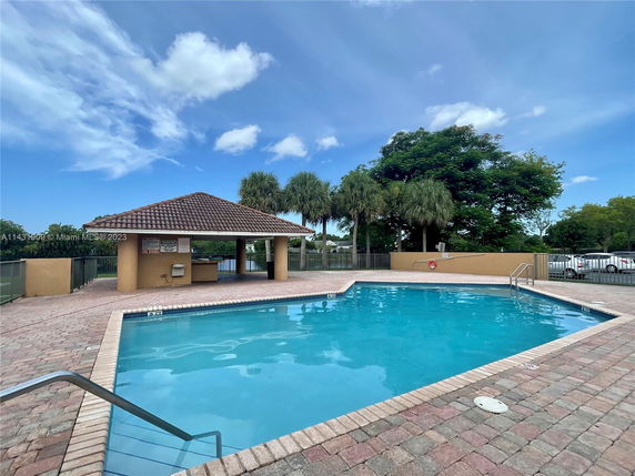 Outdoor swimming pool area with a covered cabana and surrounded by trees.