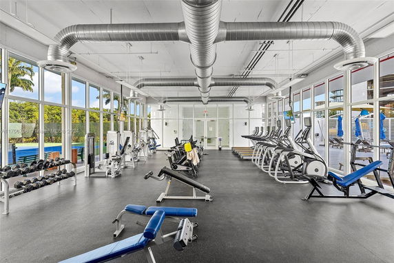Interior view of a gym with various exercise equipment and large windows.