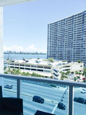 Balcony view of a high-rise building and parking structure with cityscape and water in the background.