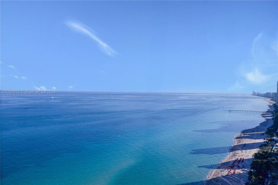 Expansive view of a coastline with clear blue water and a sandy beach lined with umbrellas.