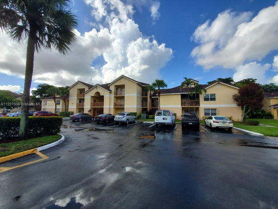 Front view of a multi-story residential building with balconies and a parking area in front.