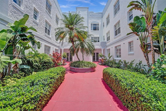 View of a building courtyard with a red walkway, surrounded by white walls and green plants.