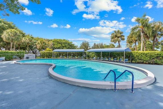 Outdoor swimming pool area with surrounding lounge chairs and palm trees.