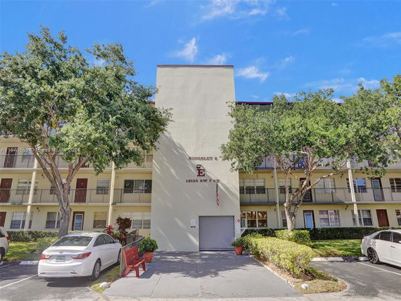 Front view of a multi-story residential building with balconies and parking spaces.